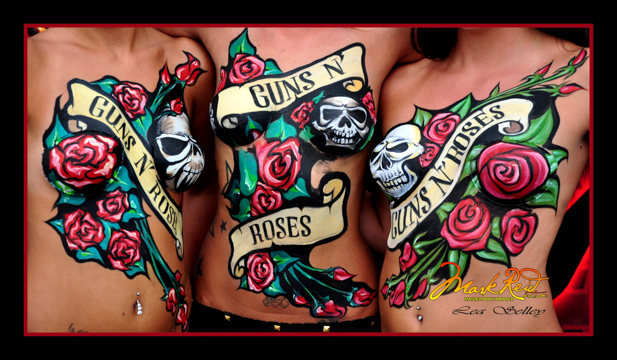 chests of three women body painted with colorful paintings on their chests each featuring a banner saying guns and roses